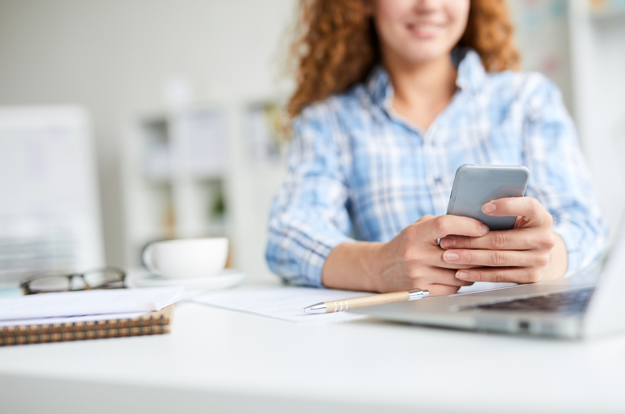 Workplace experience app. Blog image of a woman holding a mobile phone while at her office desk.